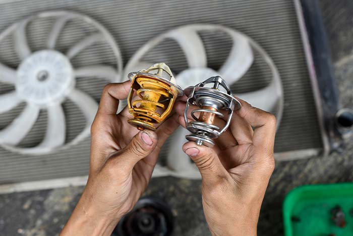 Automotive Mechanic Holding Two Engine Thermostats Comparing Old To New 