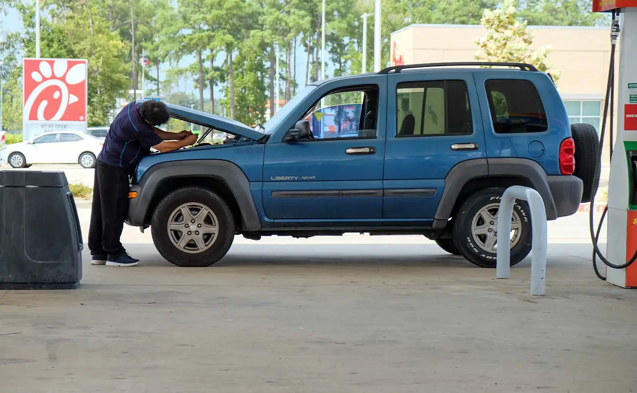 man working on his broken down car at gas station