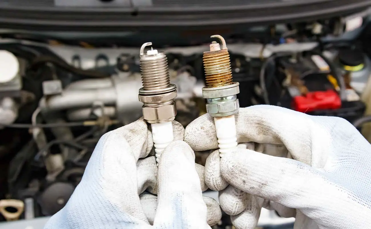 mechanic holding brand new and old spark plugs in hands