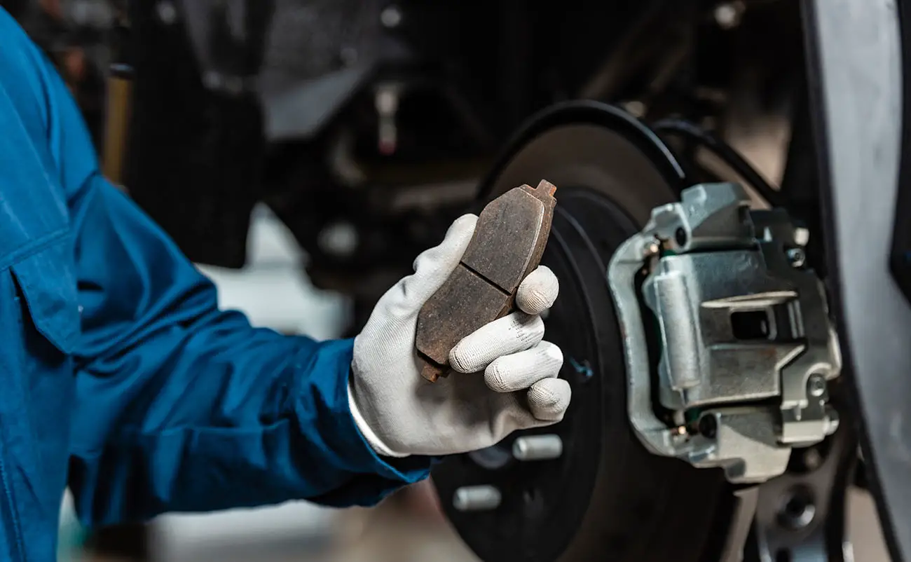 mechanic holding worn brake pad near disc brakes in background