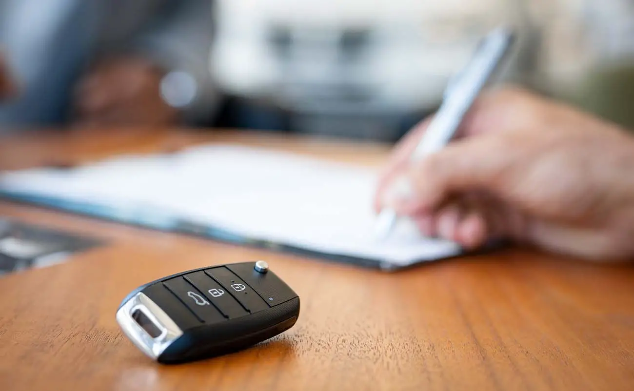 car keys on desk with man signing documents in background