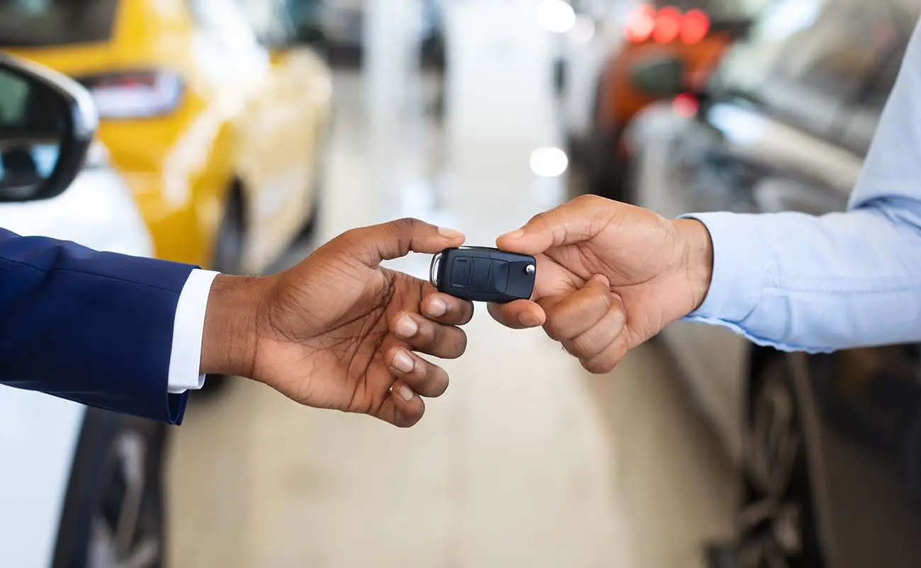 young man handing off car key to auto dealership salesman