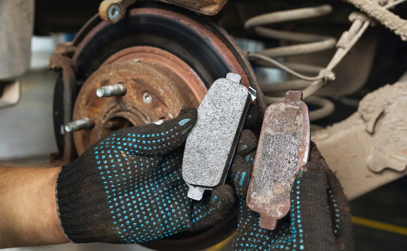 car mechanic holding new brake pad and worn brake pad in hands comparison