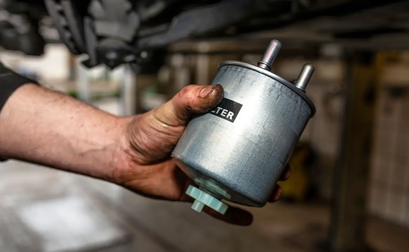 car mechanic holding new fuel filter in hand while in car workshop