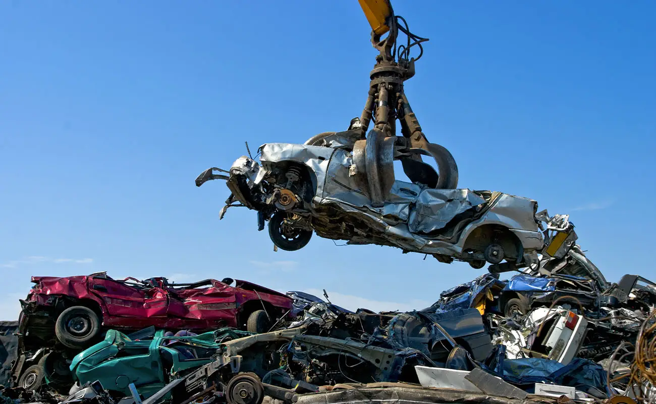 crane picking up a scrap car in a junkyard